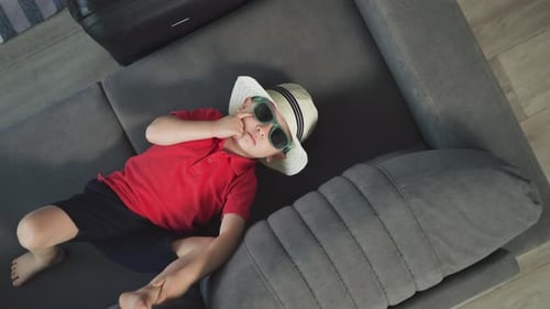 Stylish Little Boy Lies on Comfortable Couch in Hotel Suite