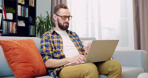Bearded Man with Laptop Typing on Sofa