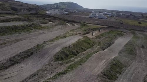 Aerial shot panning left as riders on motocross track hit a jump.