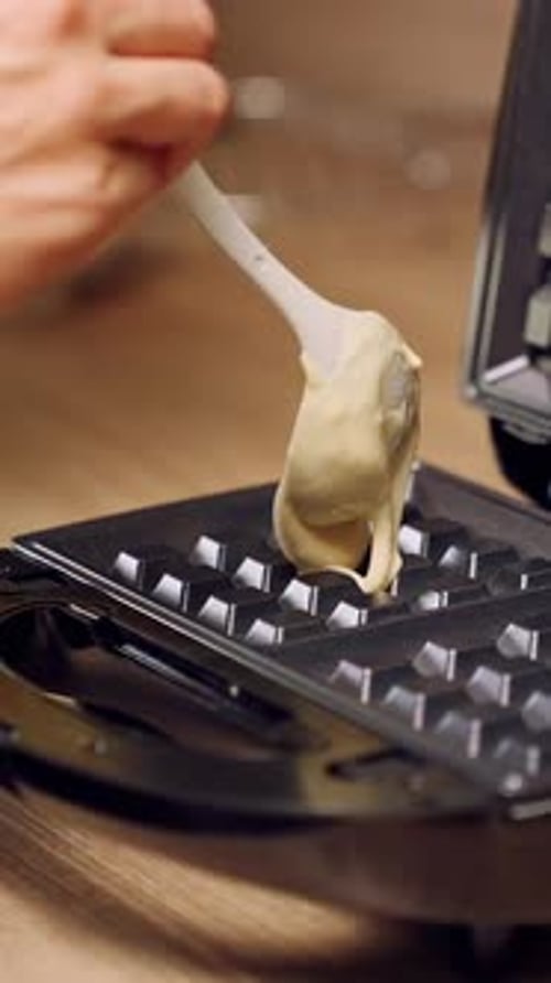 Vertical video. Slow Motion Close Up Of Spoon Pouring Thick Batter Into Open Waffle Maker On Kitchen