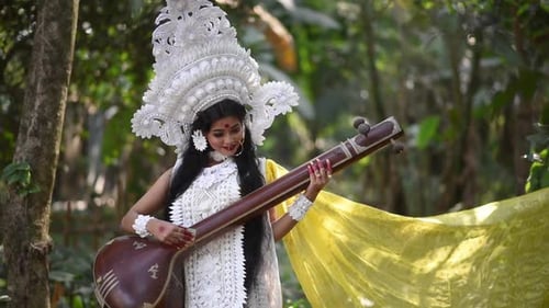 Alone Beautiful Indian girl posing as Hindu Goddess Saraswati in forest with veena, slow motion