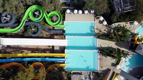 Drone hovers in a bird's eye view over a water park with slides and tennis court - people slide down
