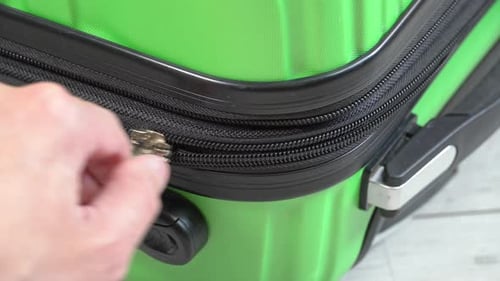 Guy opens and closes green baggage case with clothes in hand luggage zip up zipper. Man packing