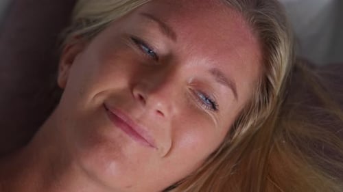 Pretty blue eyed blond woman opening eyes waking up lying in bed, fair skin caucasian