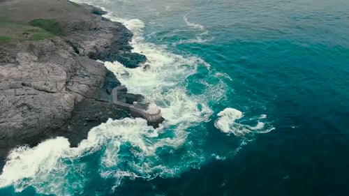 Aerial drone footage of blue and green ocean sea water hitting the shoreline where steep cliffs and