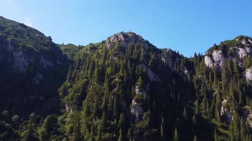 Drone View Of A Mountain Forest With High Peaks In The Background And A Clear Blue Sky