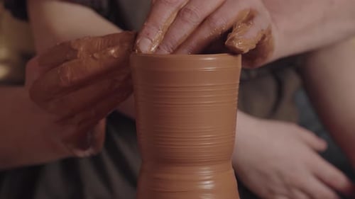 Les mains de Man Potter soutiennent une cruche rotative et l'enduisent d'une couche d'argile. Un enfant dans le dos