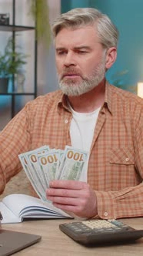 Mature Man Sitting on Sofa Table with Laptop and Calculator Managing Family Budget at Home