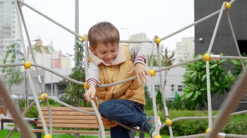 Happy cheerful boy climbing through ropes and nets on the public playground