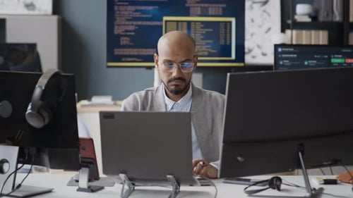 Indian Software Engineer Coding on Laptop with Multiple Monitors in Office