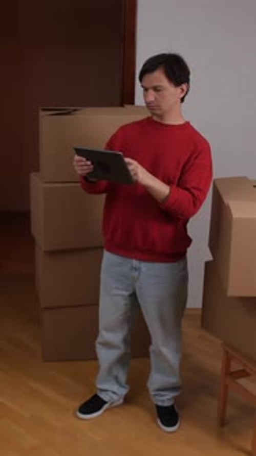 Vertical Video Closeup Man Using Digital Tablet While Organizing New Home with Cardboard Boxes