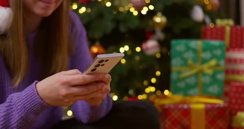 Woman Using Smartphone By Christmas Tree and Gifts