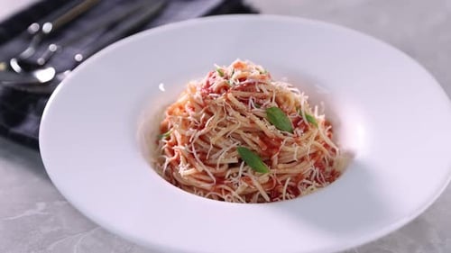 Delicious pasta with cheese, tomato sauce, basil and cutlery on grey table. Camera moving in