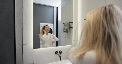 Woman Blow Drying Hair in Modern Bathroom Mirror