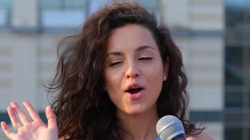 Woman Sings and Gestures with Microphone Outside