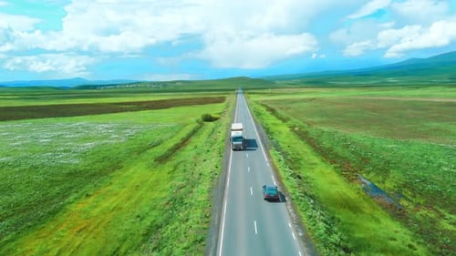 Shooting from drone shows highway among mountains of meadows. Car rushes