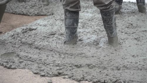 Nahaufnahme eines Arbeiters, der mit seiner Schaufel auf nassem Beton arbeitet.
