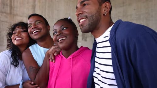 Group of four happy young friends standing together outdoors in the sunlight, laughing and smiling w