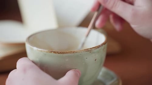 Close Up Hand Stirs Coffee in Cup on Wooden Table Indoors