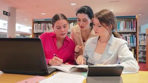 Three Young Women Studying Together in a University Library Collaborating on Assignments and