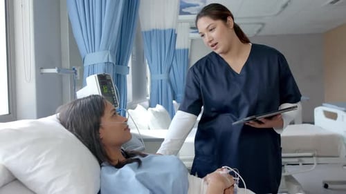 Diverse female patient in hospital bed and female doctor using tablet talking, slow motion