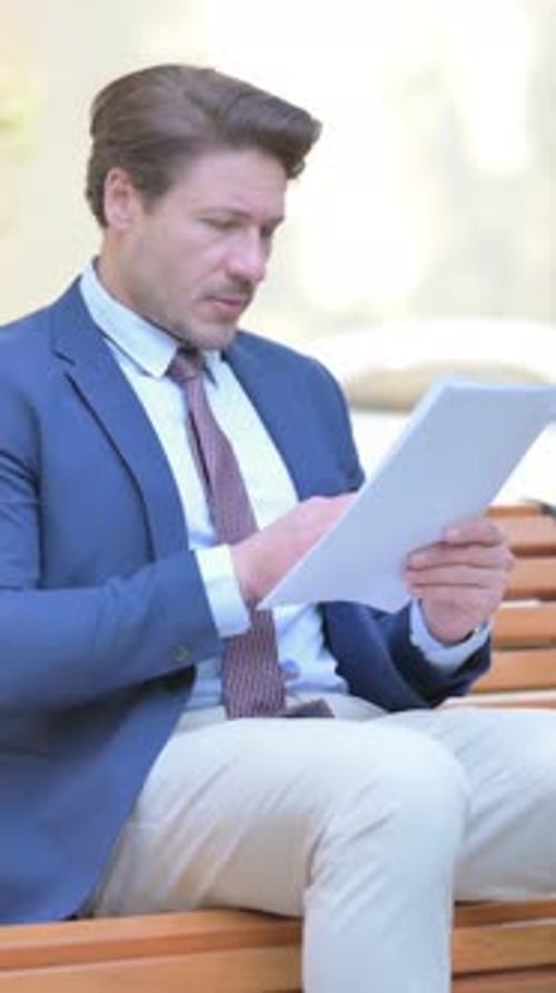 Man in Suit Reads Documents on Bench