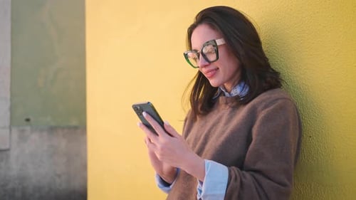 Smiling Woman Using Smartphone Against Yellow Wall