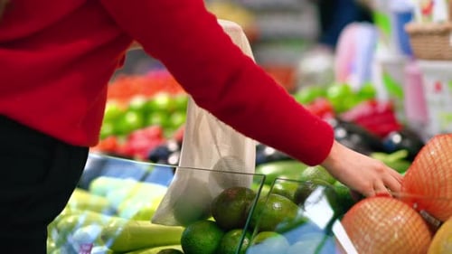 Mujer recogiendo aguacates en una bolsa reutilizable en una tienda. Temáticas del Día de la Tierra y la Ecología