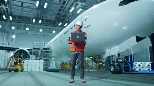 Asian Male Engineer Looking At A Laptop And Looking Around While Aircraft Maintenance