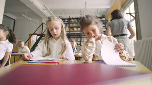 In einem Klassenzimmer der Grundschule Portrait zweier Klassenkameraden, die an der Rezeption sitzen und schreiben
