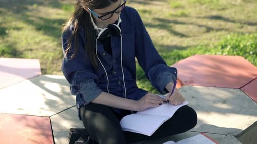 Teenage Girl Doing Homework, Writing Notes in Notepad Sitting in Park Alone