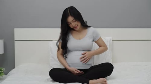 Beautiful Pregnant Woman Sitting on Bed Rubbing Belly