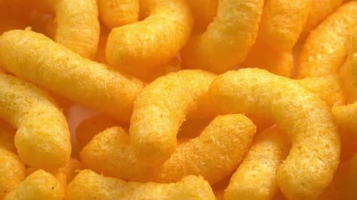 Cheesy corn sticks rotates closeup side light. Crispy cheese snack. Crispy fluffy corn chips