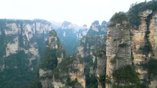 Aerial dolly between columnar towers of rock in misty canyon of Zhangjiajie China