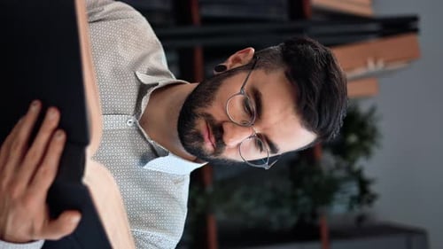 VERTICAL VIDEO POV Pensive Hispanic Man Reading Interesting Book Educational Academic Knowledge