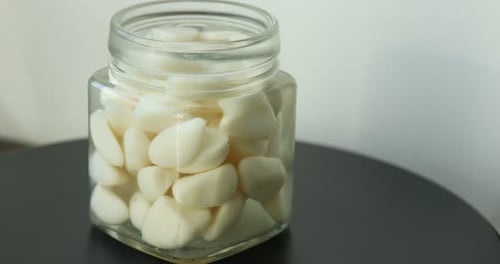 Dientes de ajo en escabeche en tarro de vidrio sobre mesa negra, primer plano