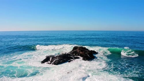 Waves crash against rocks in the middle of the ocean.