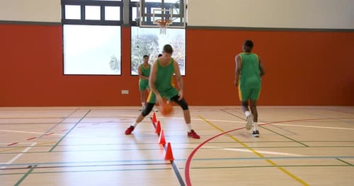 Basketball players practicing dribbling skills in gym with orange cones