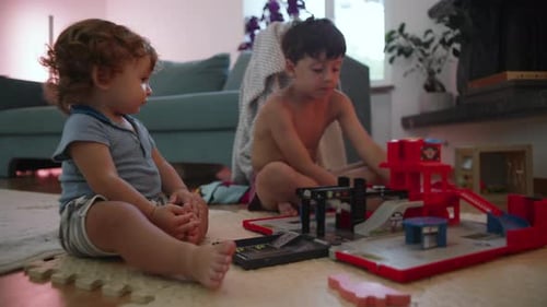 Two young brothers playing with toy cars and garage set on floor at home, childhood bonding and