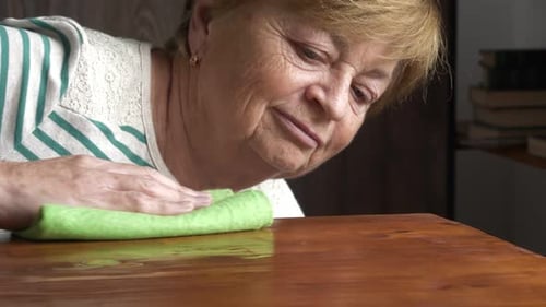Senior Woman Cleans Wooden Table with Cloth