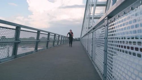 Young woman in black sport outfit running on city bridge.