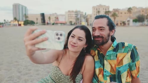 Happy couple taking selfie on mobile phone while sitting on the beach