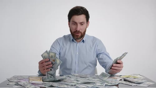 Ein Mann in einem blauen Hemd schaut in die Kamera und hält etwas Geld in der Hand, bevor er es fallen lässt