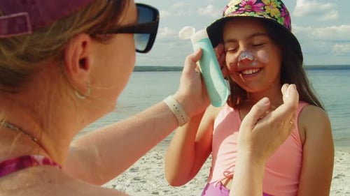 Mutter trägt Sonnencreme auf lächelnde Tochter im Strandurlaub auf