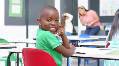 In school, smiling boy sitting at desk with notebook and pen in classroom