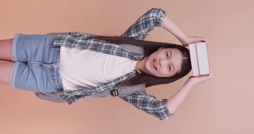Cute school girl is carrying a school bag and holding a textbook on a brown background.