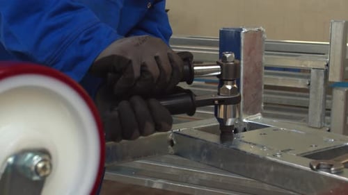 Worker making holes for screws in aluminum frame, inside workshop, handheld view