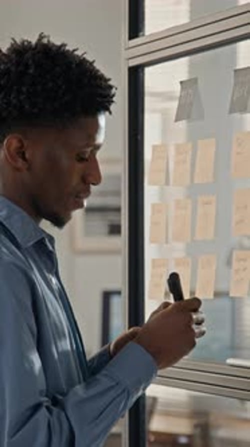 Businessman Writing Notes on Sticky Notes on Office Glass Door
