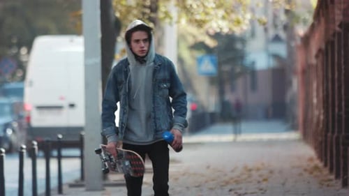 Jovem sério sobre pintar o muro da rua caminha pela cidade com skate e tinta spray