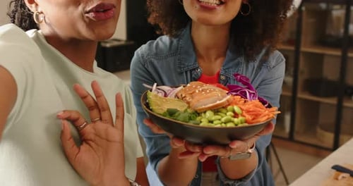 Estendendo a saladeira Poke para a câmera, diversas co-apresentadoras compartilham comentários sobre receitas na cozinha